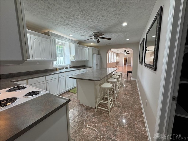 523 Newport Rd, Xenia, OH 45385 - kitchen featuring a ceiling fan, white refrigerator with ice dispenser, dark countertops, a kitchen breakfast bar, and a textured ceiling