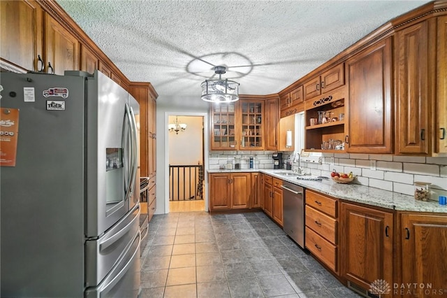 945 Oakland Dr, Beavercreek Twp, OH 45434 - kitchen featuring stainless steel appliances, a chandelier, brown cabinets, decorative backsplash, and glass insert cabinets