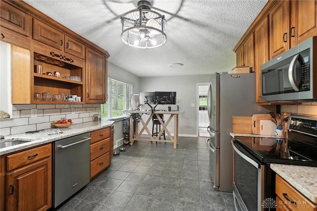 945 Oakland Dr, Beavercreek Twp, OH 45434 - kitchen with appliances with stainless steel finishes, a textured ceiling, brown cabinetry, tasteful backsplash, and light stone counters