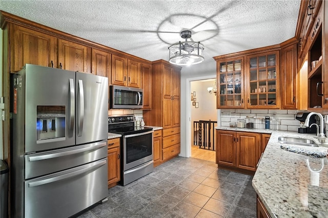 945 Oakland Dr, Beavercreek Twp, OH 45434 - kitchen featuring appliances with stainless steel finishes, backsplash, brown cabinets, glass insert cabinets, and light stone countertops