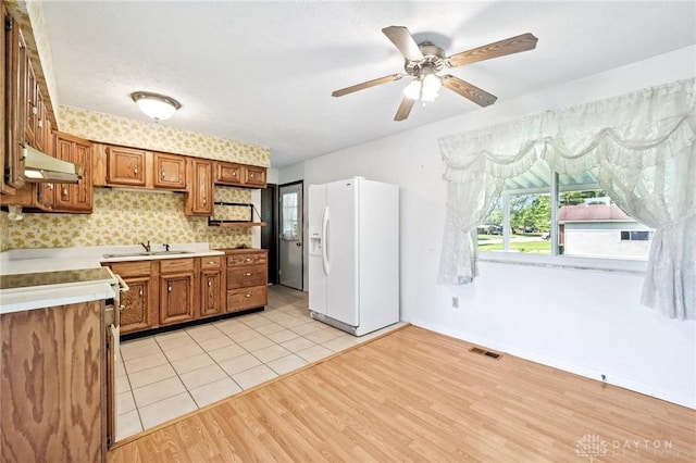 1513 Arrowhead Trl, Xenia, OH 45385 - kitchen with white refrigerator with ice dispenser, under cabinet range hood, brown cabinetry, light countertops, and ceiling fan