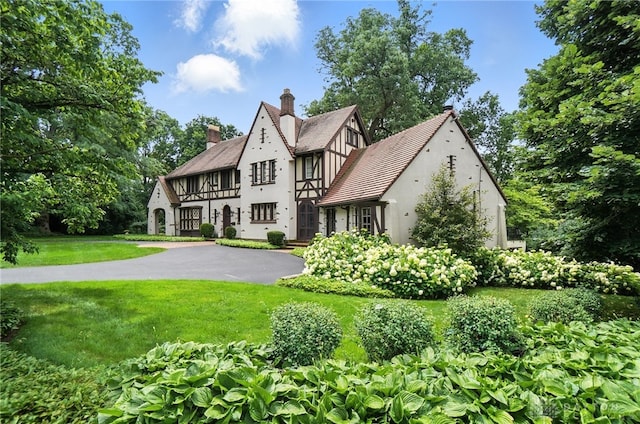 1160 Lytle Ln, Kettering, OH 45409 - tudor-style house with stucco siding, a chimney, a front yard, asphalt driveway, and a balcony