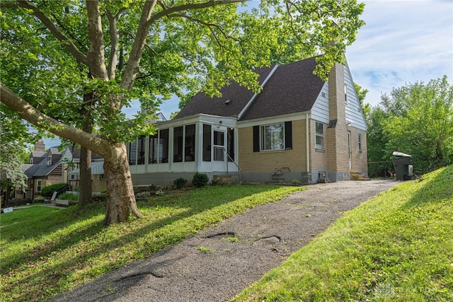 2311 Alpine Way, Dayton, OH 45406 - view of front of house with a sunroom, a shingled roof, brick siding, a front yard, and driveway