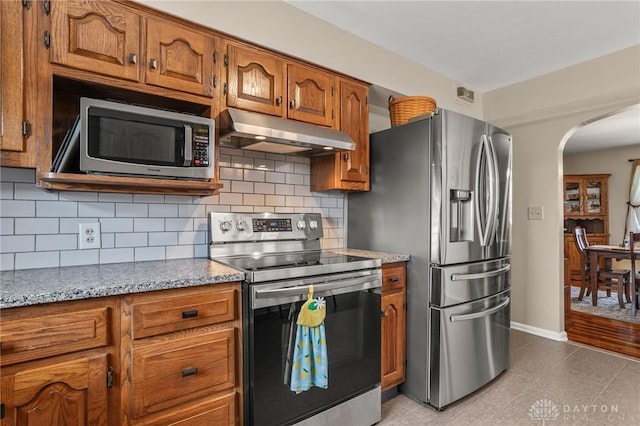 6977 Alternate State Route 49, Arcanum, OH 45304 - kitchen with appliances with stainless steel finishes, under cabinet range hood, arched walkways, brown cabinetry, and tasteful backsplash