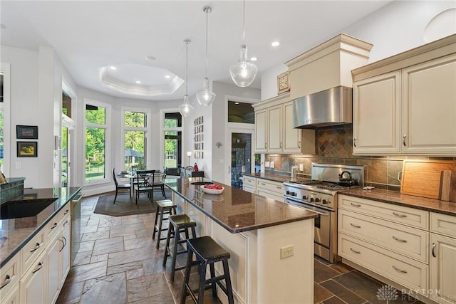 7921 Locust Grove Ct, Springboro, OH 45066 - kitchen featuring stainless steel appliances, cream cabinets, wall chimney exhaust hood, stone tile floors, and recessed lighting
