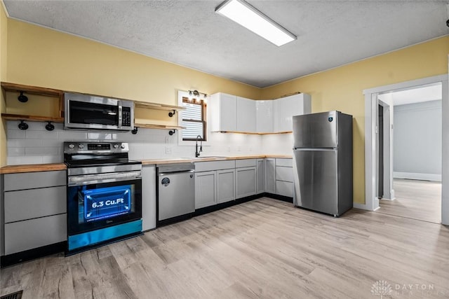 506 Virginia Ave, Troy, OH 45373 - kitchen with stainless steel appliances, open shelves, tasteful backsplash, light wood-type flooring, and a textured ceiling