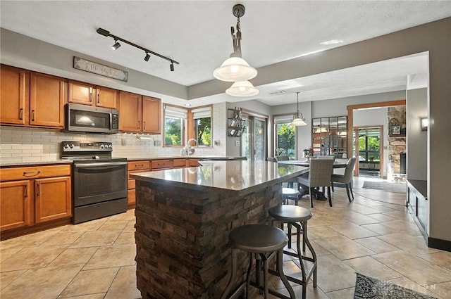 1778 Kensington Dr, Bellbrook, OH 45305 - kitchen featuring stainless steel appliances, light tile patterned flooring, brown cabinetry, decorative backsplash, and a kitchen bar
