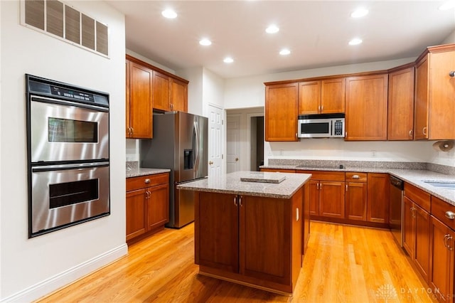 2540 Early Spring Ct, Dayton, OH 45459 - kitchen featuring stainless steel appliances, light wood-type flooring, a kitchen island, light stone counters, and brown cabinetry