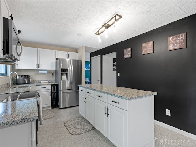 6118 Carnation Rd, Dayton, OH 45449 - kitchen with stainless steel appliances, a kitchen island, white cabinets, a textured ceiling, and light stone counters