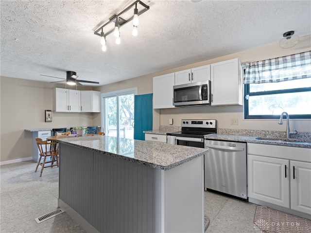 6118 Carnation Rd, Dayton, OH 45449 - kitchen with appliances with stainless steel finishes, a kitchen island, white cabinetry, light stone countertops, and a textured ceiling