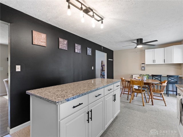 6118 Carnation Rd, Dayton, OH 45449 - kitchen with a textured ceiling, a ceiling fan, white cabinetry, a center island, and light stone counters