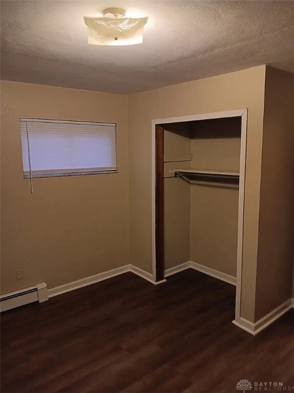 4129 E 3rd St Unit 4127, Dayton, OH 45403 - unfurnished bedroom featuring a baseboard heating unit, wood finished floors, a closet, and a textured ceiling