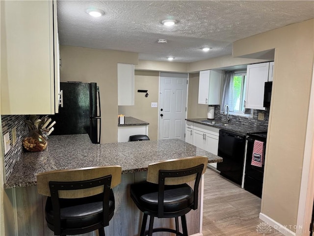 6346 Apache St, Dayton, OH 45424 - kitchen with black appliances, a peninsula, a kitchen breakfast bar, white cabinetry, and decorative backsplash