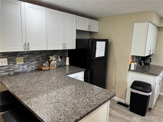 6346 Apache St, Dayton, OH 45424 - kitchen with light wood finished floors, dark stone countertops, backsplash, white cabinetry, and a peninsula