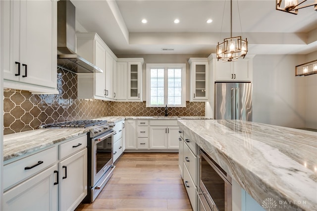 1461 Abbey Park Pl, Beavercreek Twp, OH 45385 - kitchen with wall chimney exhaust hood, appliances with stainless steel finishes, light wood-style floors, light stone counters, and white cabinetry
