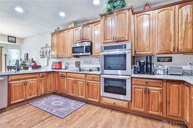 595 Heatherwoode Cir, Springboro, OH 45066 - kitchen featuring appliances with stainless steel finishes, a textured ceiling, light stone counters, light wood finished floors, and recessed lighting