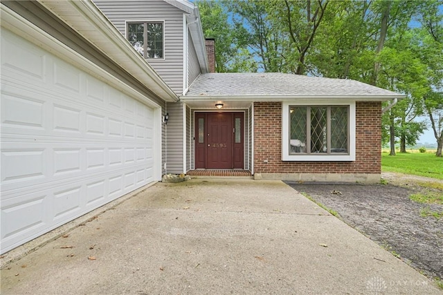 4595 Comanchee Trl, Silver Creek Twp, OH 45335 - view of exterior entry with driveway, a chimney, brick siding, and a shingled roof