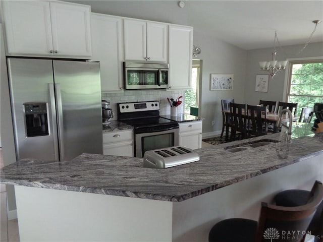 12071 Oxford Rd, Germantown, OH 45327 - kitchen with stainless steel appliances, a chandelier, white cabinetry, decorative backsplash, and a breakfast bar area