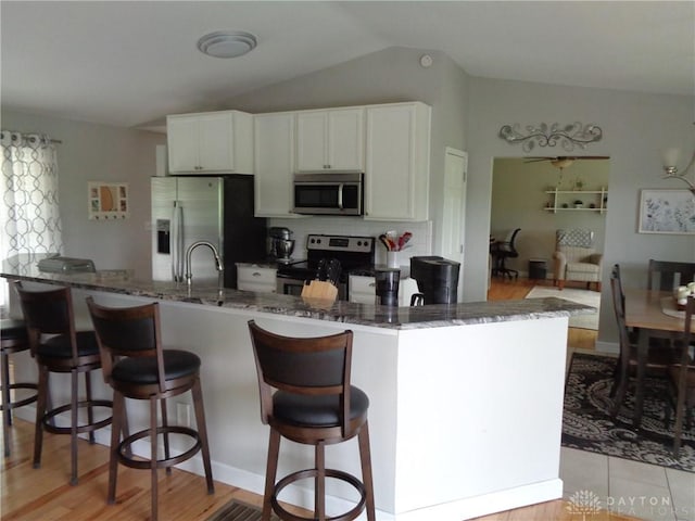 12071 Oxford Rd, Germantown, OH 45327 - kitchen featuring stainless steel appliances, dark stone counters, vaulted ceiling, a breakfast bar, and white cabinets
