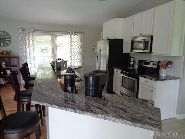 12071 Oxford Rd, Germantown, OH 45327 - kitchen with stainless steel appliances, white cabinets, backsplash, dark stone countertops, and a kitchen bar