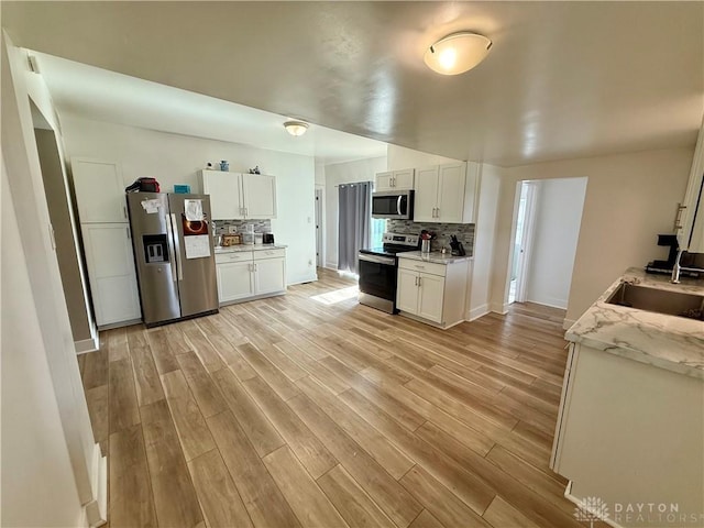 10995 Rockridge Rd, Lewisburg, OH 45338 - kitchen with appliances with stainless steel finishes, decorative backsplash, light wood-type flooring, white cabinetry, and light stone counters