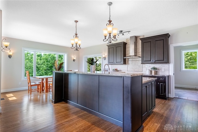 1590 Fairground Rd, Xenia, OH 45385 - kitchen with wall chimney range hood, a chandelier, decorative backsplash, dark wood finished floors, and a center island with sink
