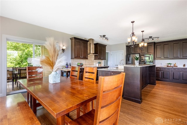 1590 Fairground Rd, Xenia, OH 45385 - kitchen with stainless steel appliances, a chandelier, wall chimney exhaust hood, dark brown cabinetry, and light wood-type flooring