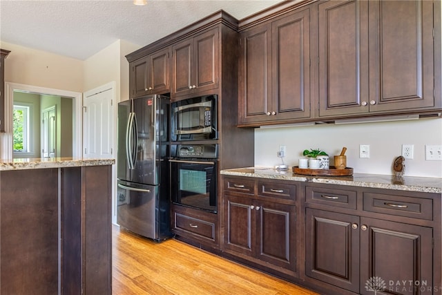 1590 Fairground Rd, Xenia, OH 45385 - kitchen with freestanding refrigerator, black oven, built in microwave, light wood finished floors, and light stone counters