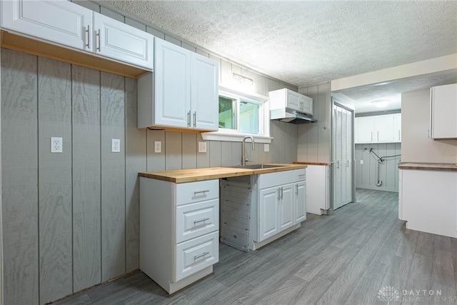 989 Ogden Rd, Adams Twp, OH 45177 - kitchen with butcher block counters, light wood-style flooring, a textured ceiling, white cabinets, and custom exhaust hood