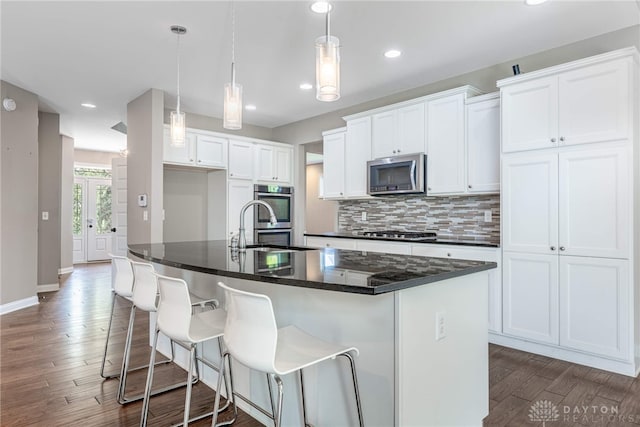 225 Woodstream Dr, Springboro, OH 45066 - kitchen with appliances with stainless steel finishes, dark countertops, dark wood-style flooring, white cabinetry, and a center island with sink
