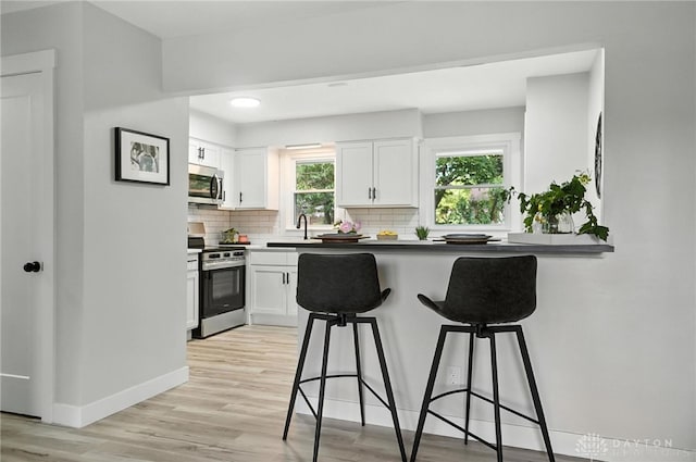 1378 Standish Ave, Riverside, OH 45432 - kitchen featuring appliances with stainless steel finishes, a breakfast bar area, backsplash, light wood finished floors, and white cabinets
