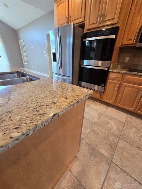 1962 Fountain View Dr, Dayton, OH 45414 - kitchen featuring appliances with stainless steel finishes, light stone counters, light tile patterned floors, lofted ceiling, and brown cabinetry