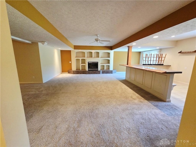 1962 Fountain View Dr, Dayton, OH 45414 - unfurnished living room featuring light colored carpet, a textured ceiling, built in shelves, a ceiling fan, and a glass covered fireplace