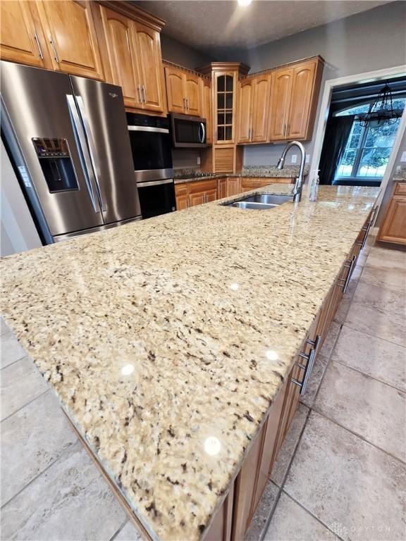 1962 Fountain View Dr, Dayton, OH 45414 - kitchen featuring stainless steel appliances, light stone counters, a large island with sink, glass insert cabinets, and brown cabinets