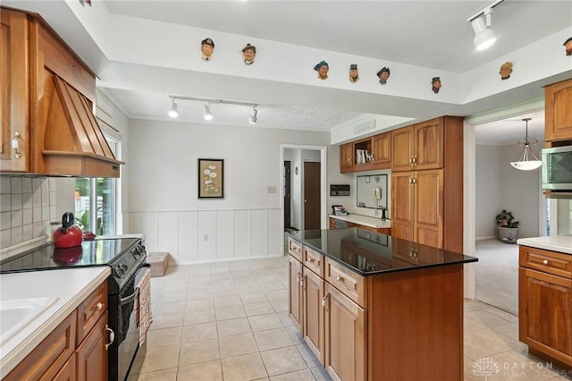 328 Shadywood Dr, Clayton, OH 45415 - kitchen with rail lighting, black range with electric stovetop, stainless steel microwave, brown cabinetry, and a wainscoted wall