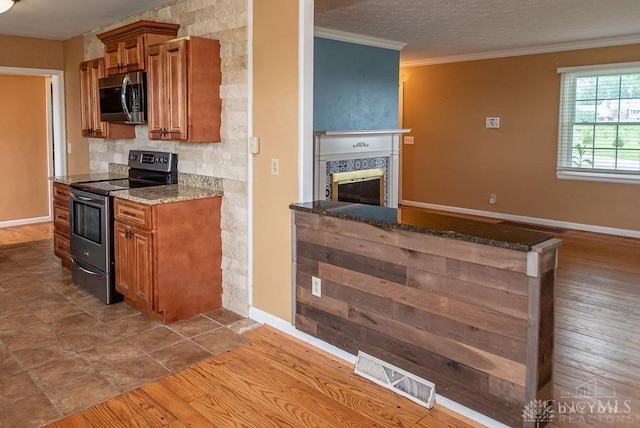 557 W N Bend Rd, Springfield Twp, OH 45224 - kitchen featuring appliances with stainless steel finishes, brown cabinetry, stone counters, a glass covered fireplace, and ornamental molding