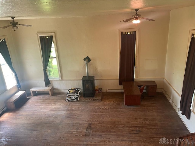 6008 Delisle-Fourman Rd, Arcanum, OH 45304 - unfurnished living room with ceiling fan, a wood stove, dark wood-style flooring, wainscoting, and a baseboard heating unit