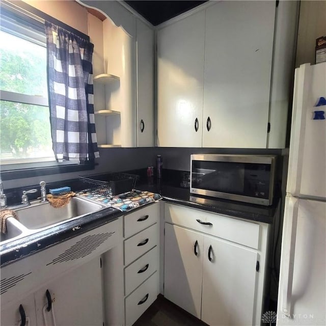 300 S Evans St, Saratoga, IN 47382 - kitchen with stainless steel microwave, freestanding refrigerator, dark countertops, white cabinets, and open shelves