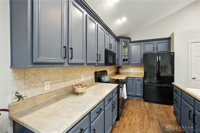 2210 Hidden Woods Blvd, Beavercreek, OH 45431 - kitchen featuring black appliances, vaulted ceiling, light countertops, dark wood finished floors, and glass insert cabinets
