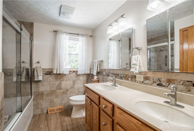 429 Rader Dr, Vandalia, OH 45377 - bathroom featuring tile walls, double vanity, shower / bath combination with glass door, wood finished floors, and a wainscoted wall