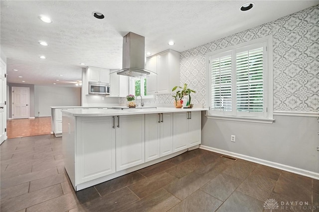 1572 Frontier Ct, Dayton, OH 45458 - kitchen featuring wallpapered walls, stainless steel microwave, a peninsula, island range hood, and recessed lighting