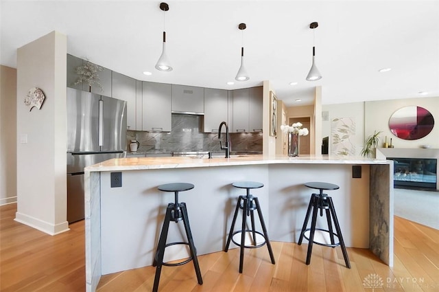 525 Heatherwoode Cir, Springboro, OH 45066 - kitchen featuring freestanding refrigerator, gray cabinets, a breakfast bar area, light wood-style floors, and decorative backsplash