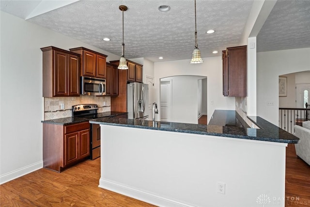 2073 Lincolnshire Dr, Beavercreek, OH 45434 - kitchen with stainless steel appliances, arched walkways, light wood-style flooring, tasteful backsplash, and a peninsula