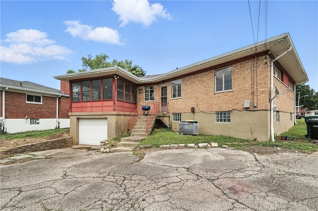 6101 Capri Dr, Cincinnati, OH 45224 - rear view of house with an attached garage, asphalt driveway, brick siding, and a sunroom