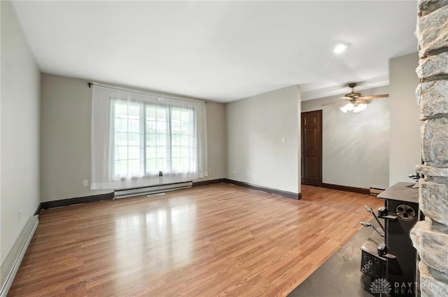 2042 Hilltop Rd, Xenia, OH 45385 - unfurnished living room with baseboard heating, ceiling fan, wood finished floors, and a wood stove