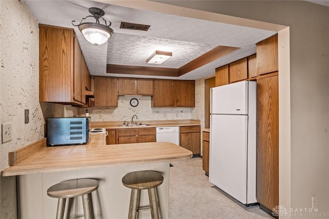 8869 Washington Colony Dr, Dayton, OH 45458 - kitchen with white appliances, light countertops, a raised ceiling, brown cabinetry, and a peninsula