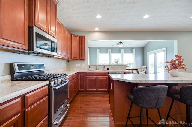 2937 E Ambrosia Ln, Xenia, OH 45385 - kitchen featuring appliances with stainless steel finishes, a kitchen bar, light countertops, dark wood-style flooring, and ceiling fan