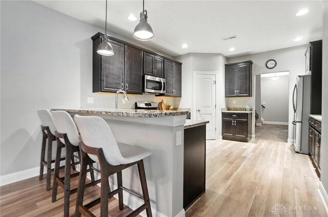 1310 Bourdeaux Way, Clearcreek Twp, OH 45458 - kitchen with a peninsula, light wood-style floors, stainless steel appliances, a kitchen bar, and pendant lighting
