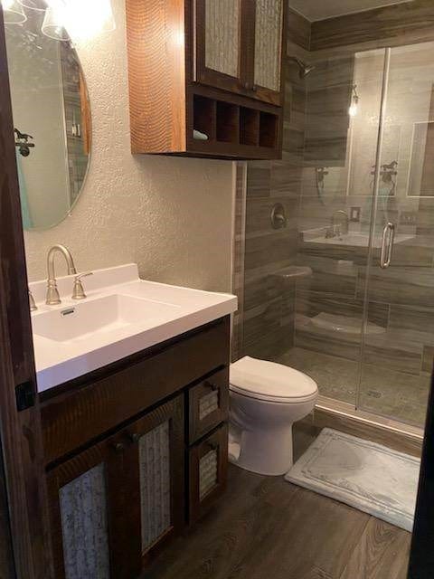 bathroom with hardwood / wood-style floors, vanity, toilet, and walk in shower