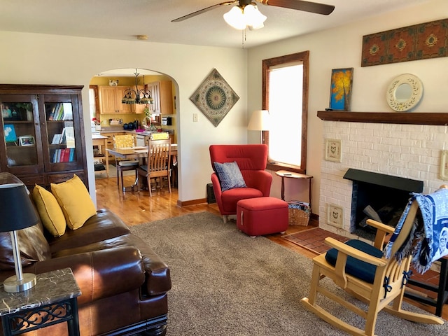 living room with wood finished floors, baseboards, a ceiling fan, a fireplace, and arched walkways